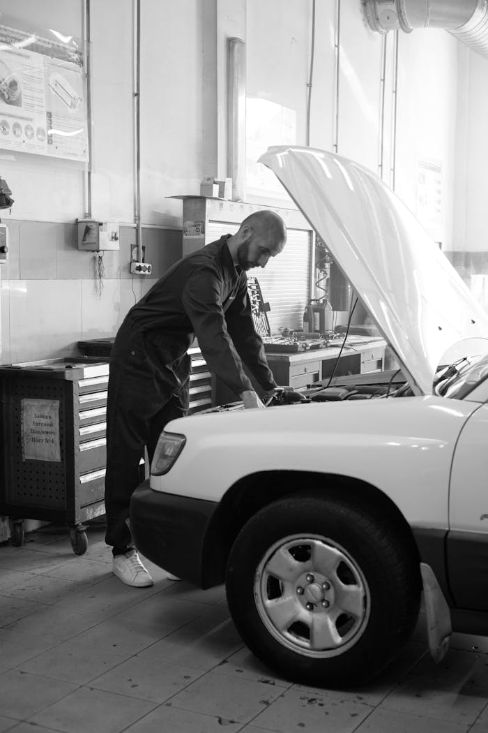 Mechanic in coverall inspecting a car engine inside a well-lit workshop.