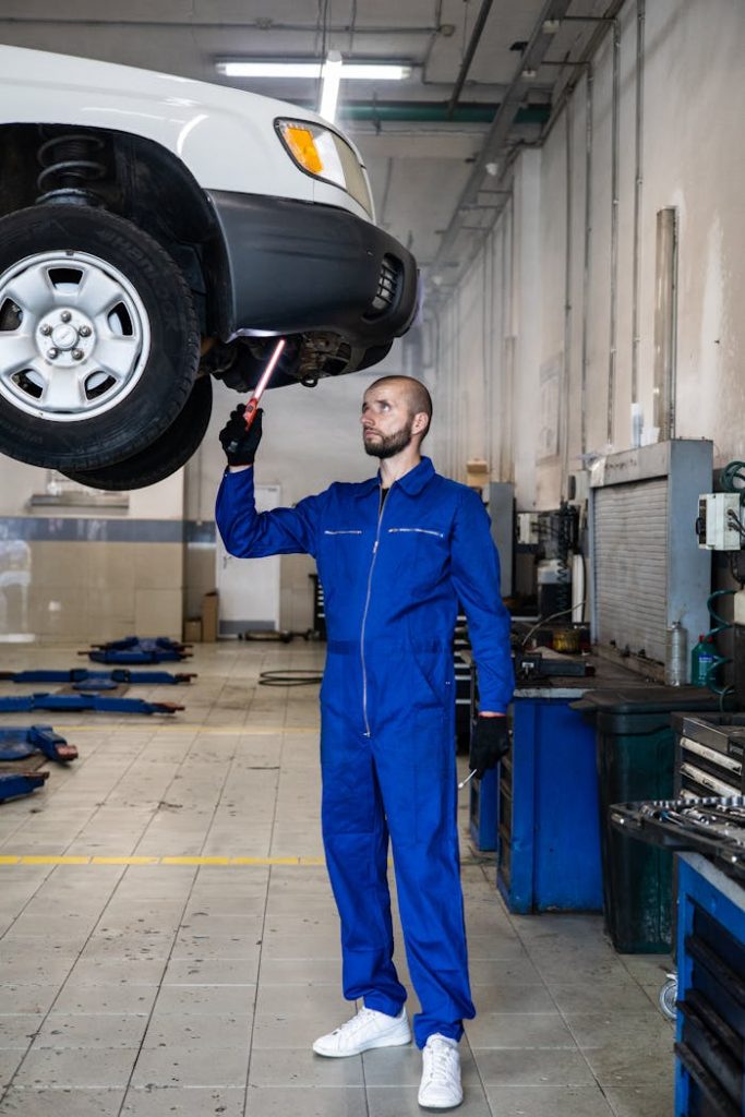 Mechanic in blue coverall inspecting car in auto repair shop. Professional vehicle maintenance in progress.